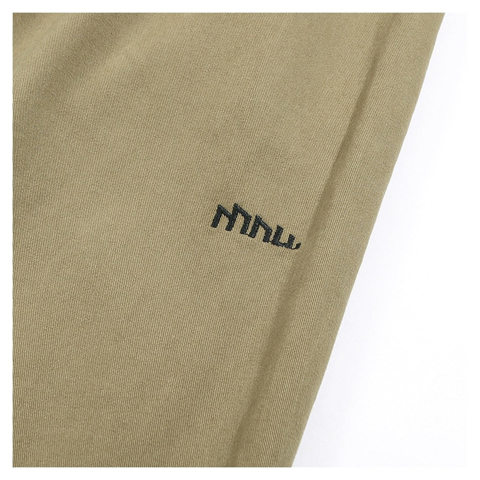 Close-up of khaki trouser fabric with a small dark embroidered mark.