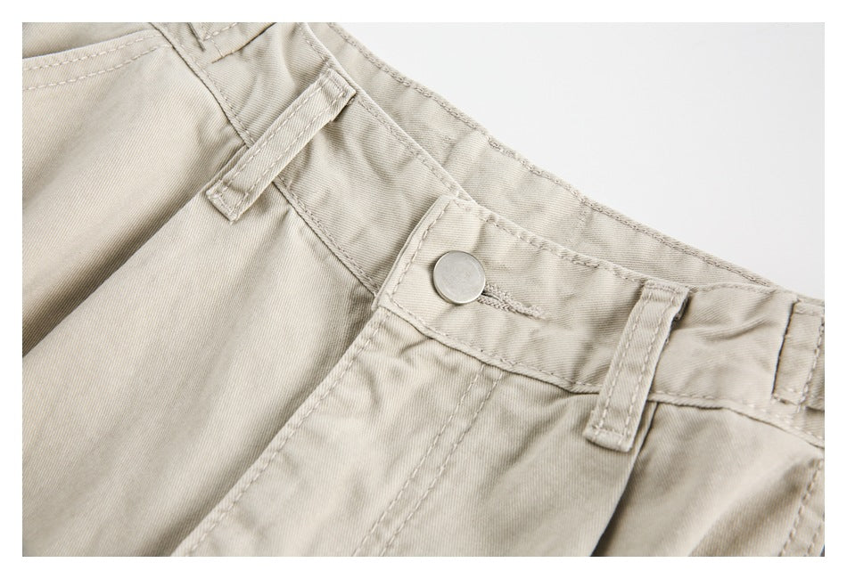 Close-up of the beige trousers' front waistband, metal button, belt loops, and stitched seam.