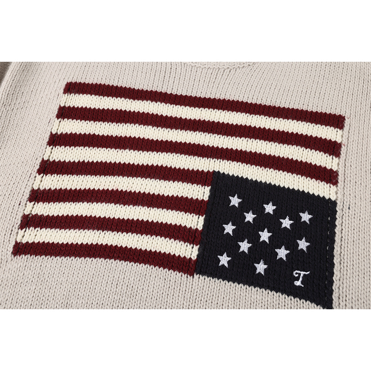 Close-up of a cream knit sweater with a burgundy, cream, and navy flag motif with white stars.