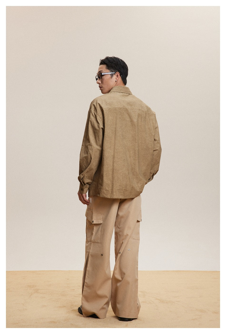 Model turned away to show the back of a tan shirt jacket with beige cargo pants.