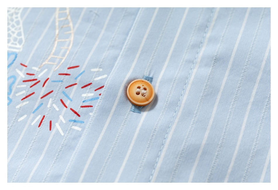Close-up of a light blue pinstriped garment with a tan button and colorful stitched-looking decorative marks.