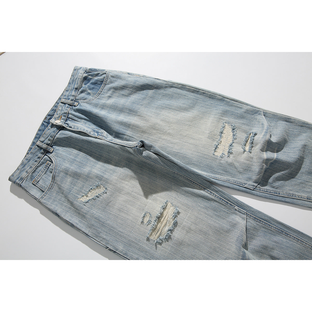 Angled close view of light-wash jeans with several frayed distressed patches across the legs.