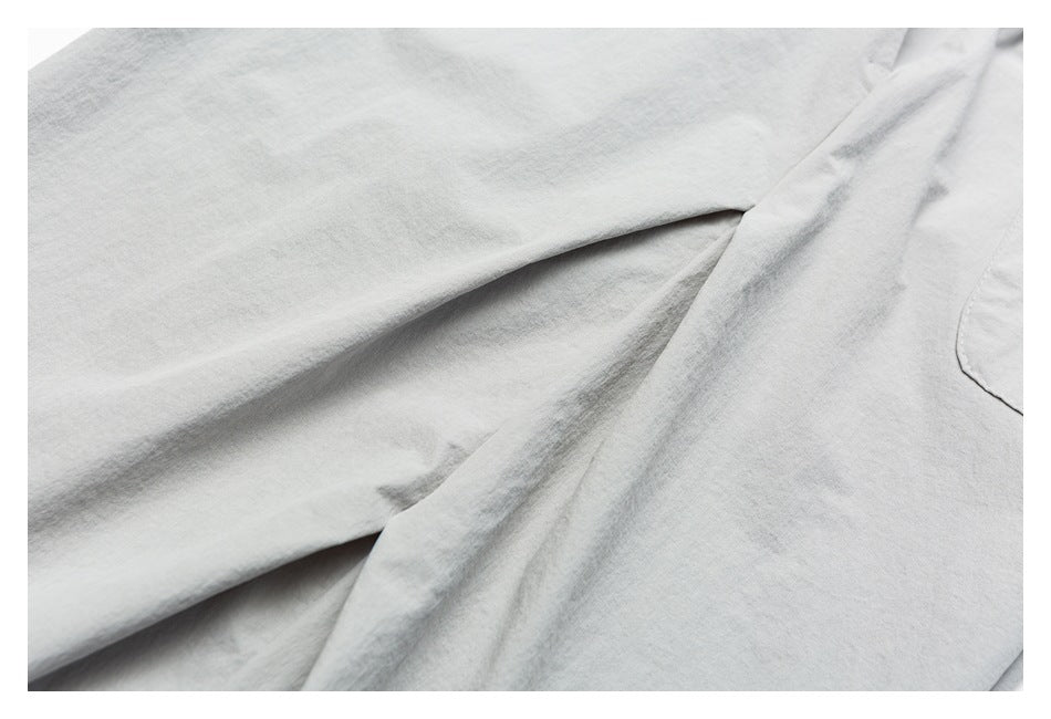 Close-up of light gray shorts fabric with a folded seam and the edge of a patch pocket.