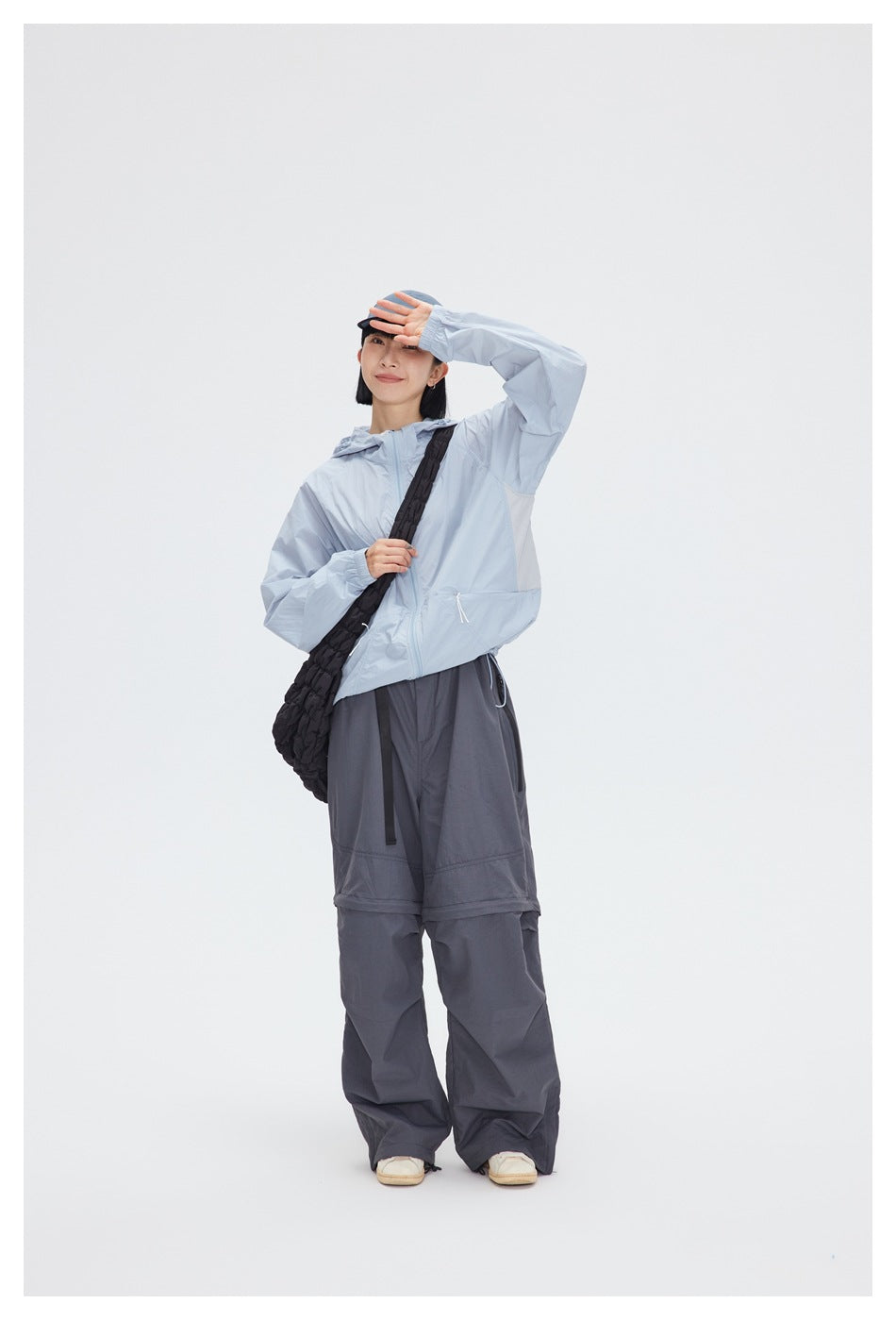 Full-length model wearing a pale blue hooded jacket, dark wide-leg pants, and a black crossbody bag.