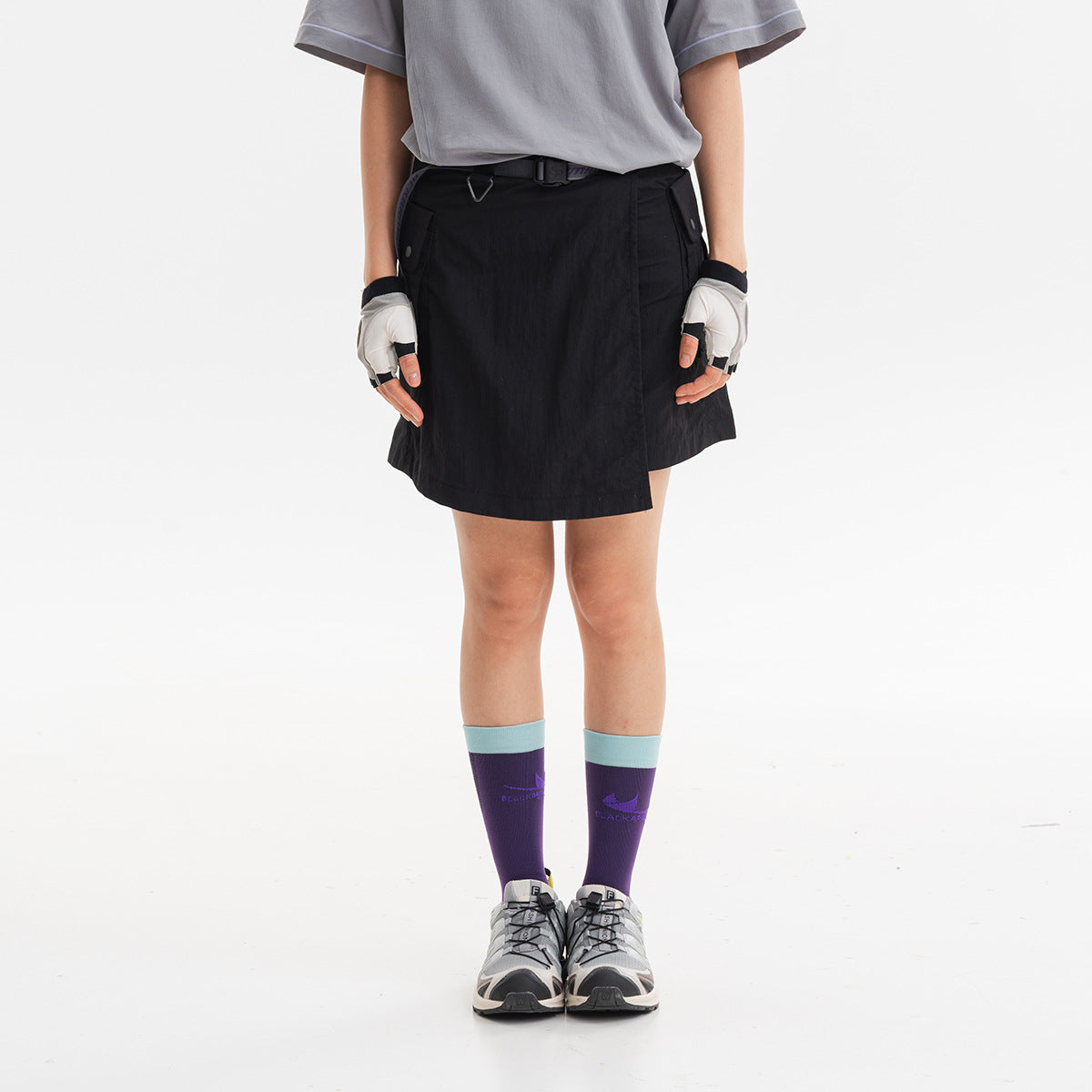 Front view of a model wearing a black utility skirt with a belt and angled wrap front.