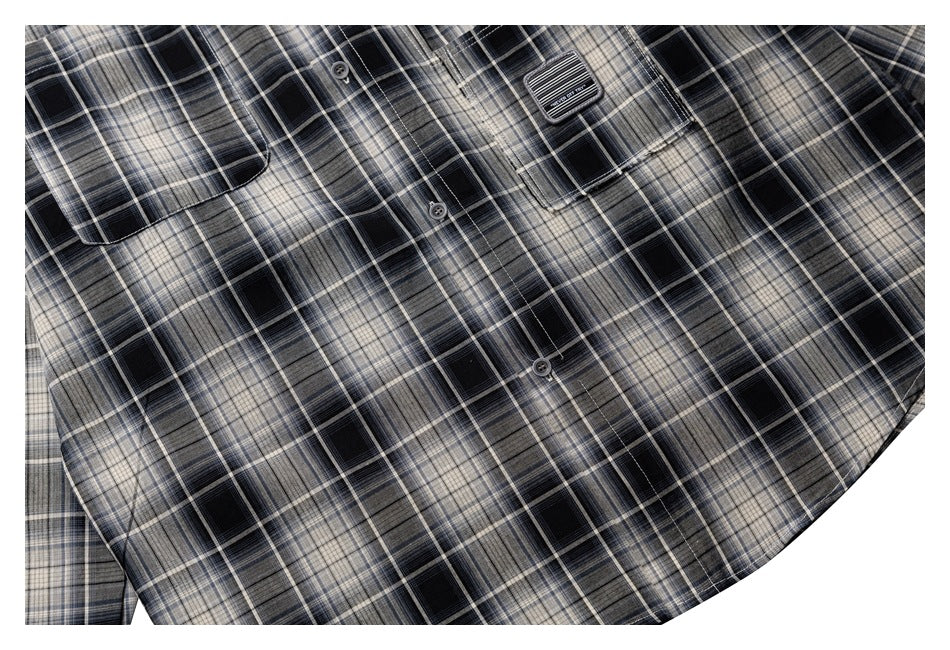 Cropped view of the front of a black, gray, and cream plaid shirt with buttons and two chest pockets.
