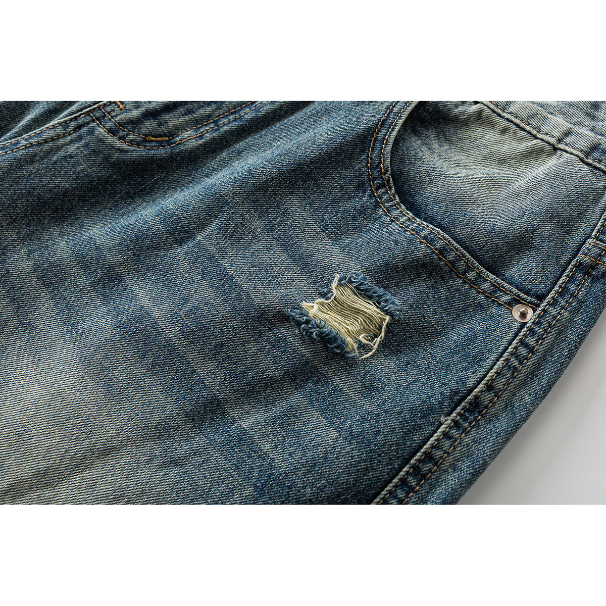 Close-up of faded blue jeans with a small frayed knee-style rip and curved pocket seam.