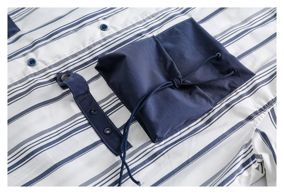 Close-up of a striped white shirt with navy buttons and a navy flap pocket with drawcords.