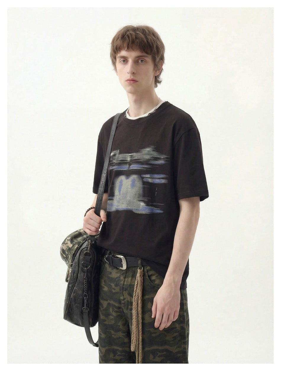 Model standing in a black short-sleeve T-shirt with an abstract blue-gray chest graphic.