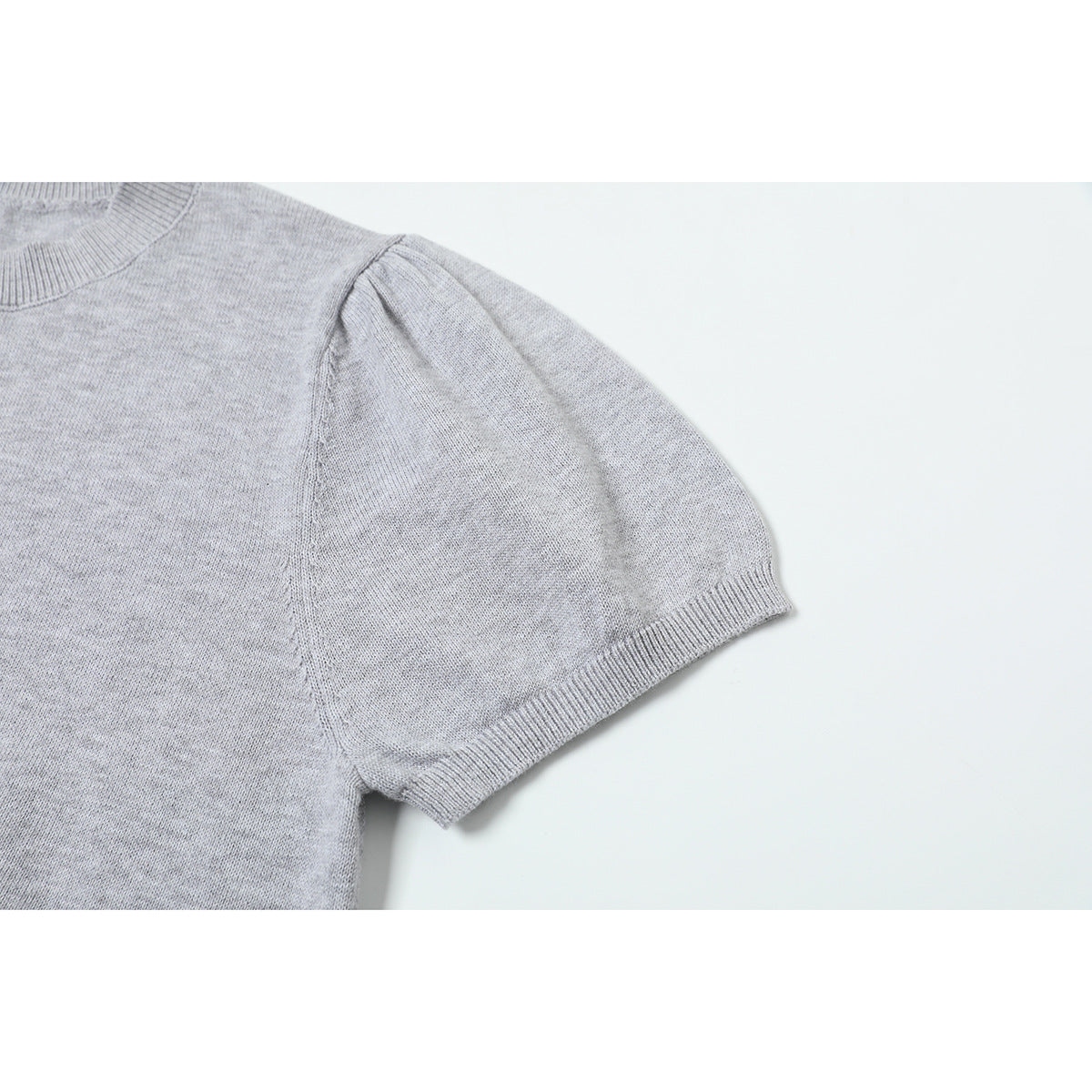 Close-up of a short puff sleeve and ribbed cuff on a light gray knit sweater.