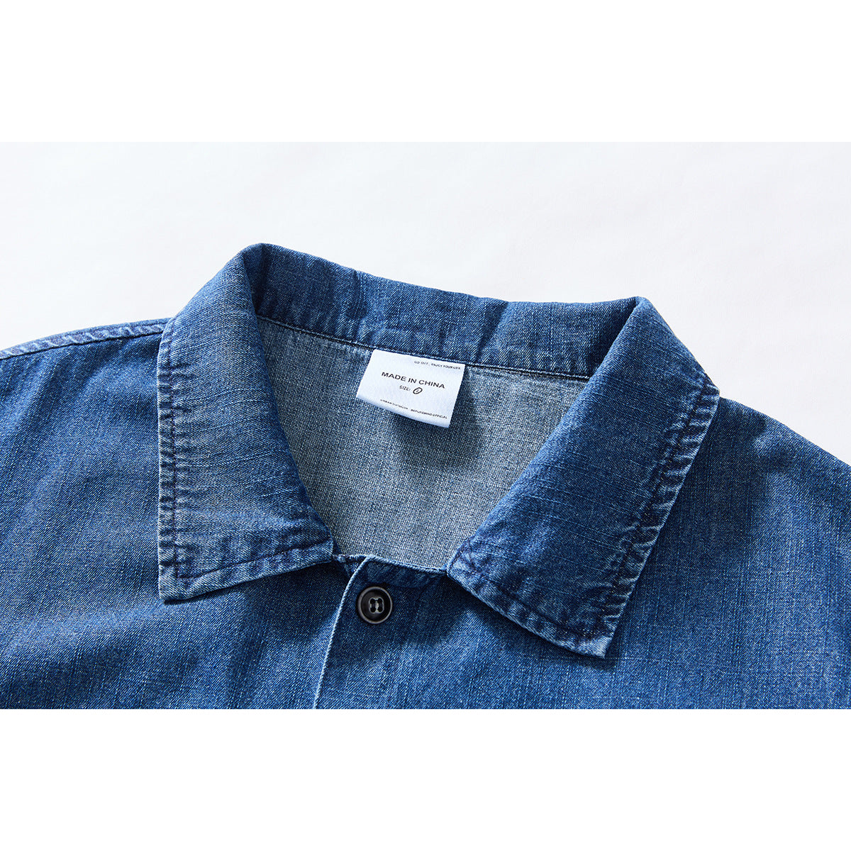 Close-up of a blue denim shirt collar, top button and sewn-in label reading “Made in China.”