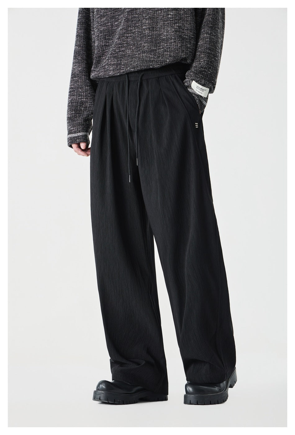 Model wearing black wide-leg pleated drawstring pants with a gray knit sweater and chunky black boots, front view