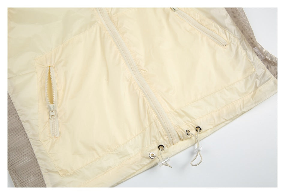 Close-up of the pale cream jacket's lower front, zip pockets, mesh side panels and adjustable hem.