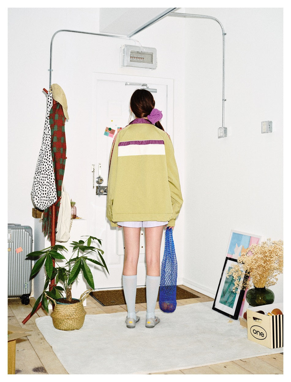 Back view of a model in an olive green track jacket with plum and cream upper-back color-block panel