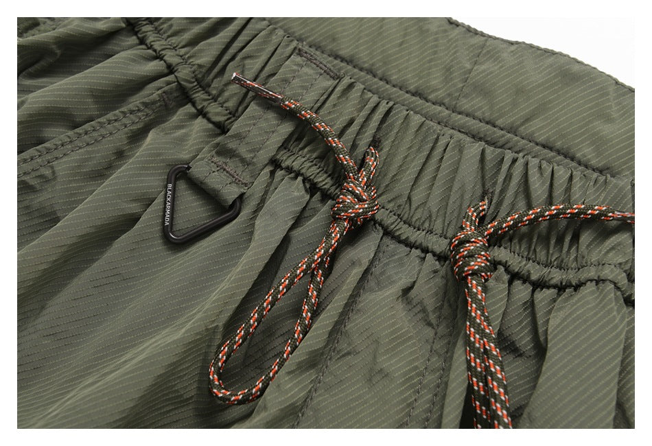 Close-up of olive shorts with a gathered waistband, orange-and-black drawcords, and a black triangular clip.