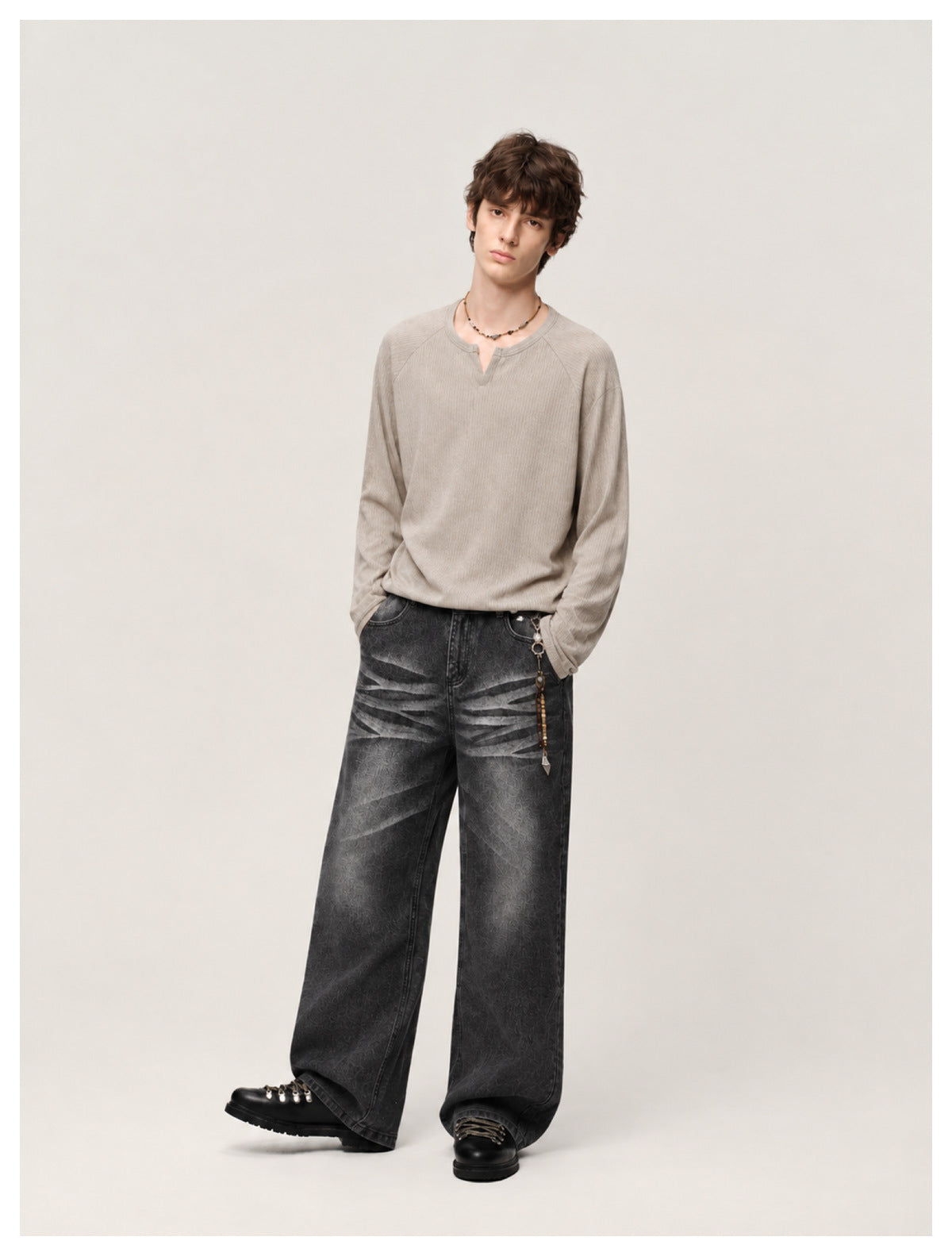 Model wearing washed black wide-leg jeans with a taupe long-sleeve top and black lace-up boots, hand in pocket
