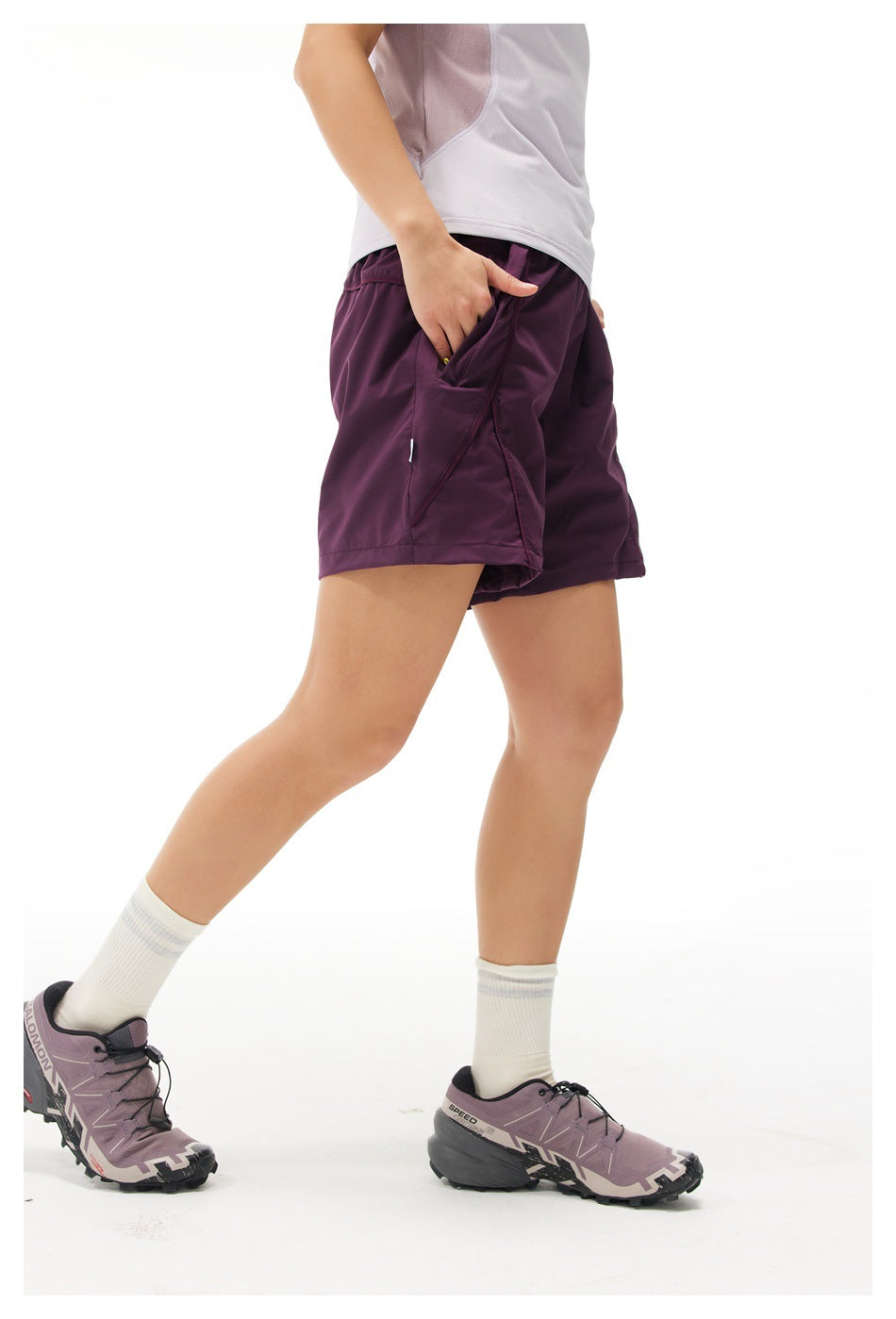 Cropped side view of a model wearing plum athletic shorts with a large pocket and yellow zipper pull.