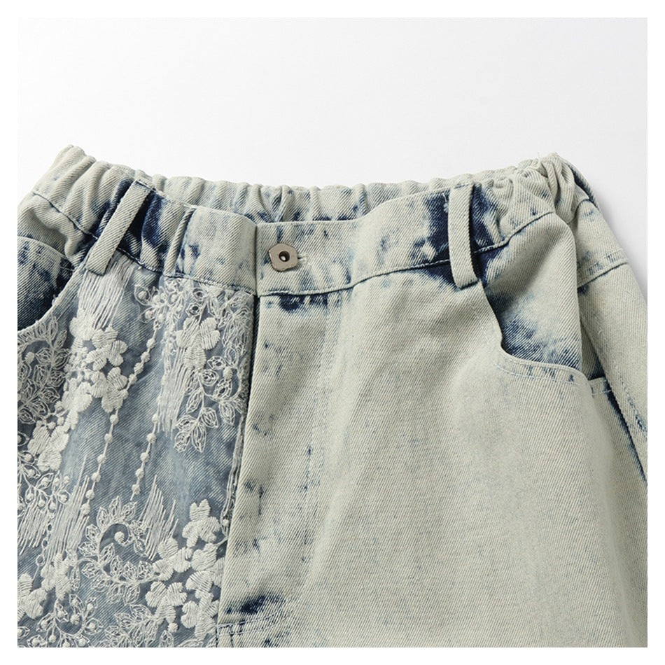 Close-up of the gathered waistband, button, pocket, and white floral embroidery on pale blue denim shorts.