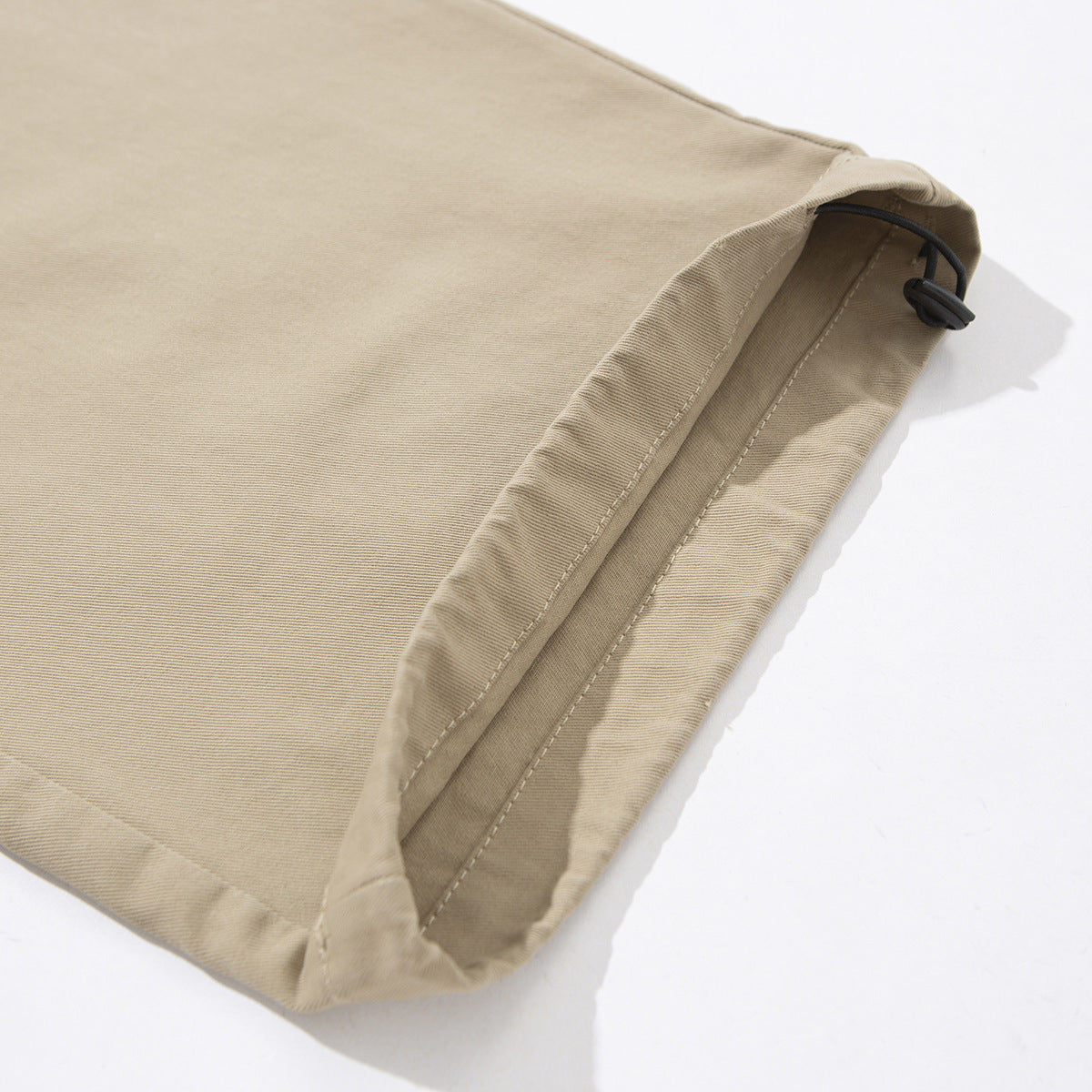 Close-up of a beige pant leg hem with a black adjustable drawcord and toggle.