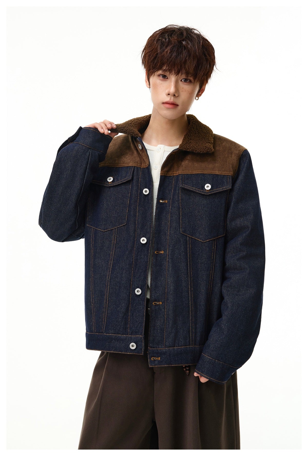 Model wearing a dark denim jacket with brown shoulder panels, sherpa collar, contrast stitching, and buttoned chest pockets.