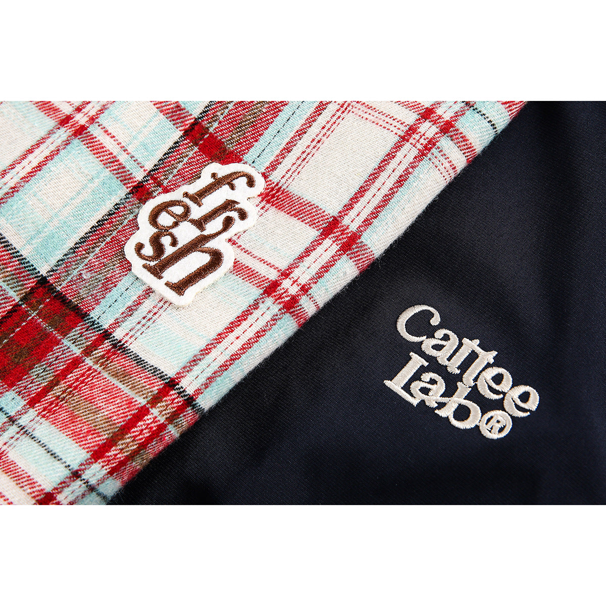 Close-up of red and pale blue plaid fabric beside navy fabric, showing embroidered logos on the jacket.