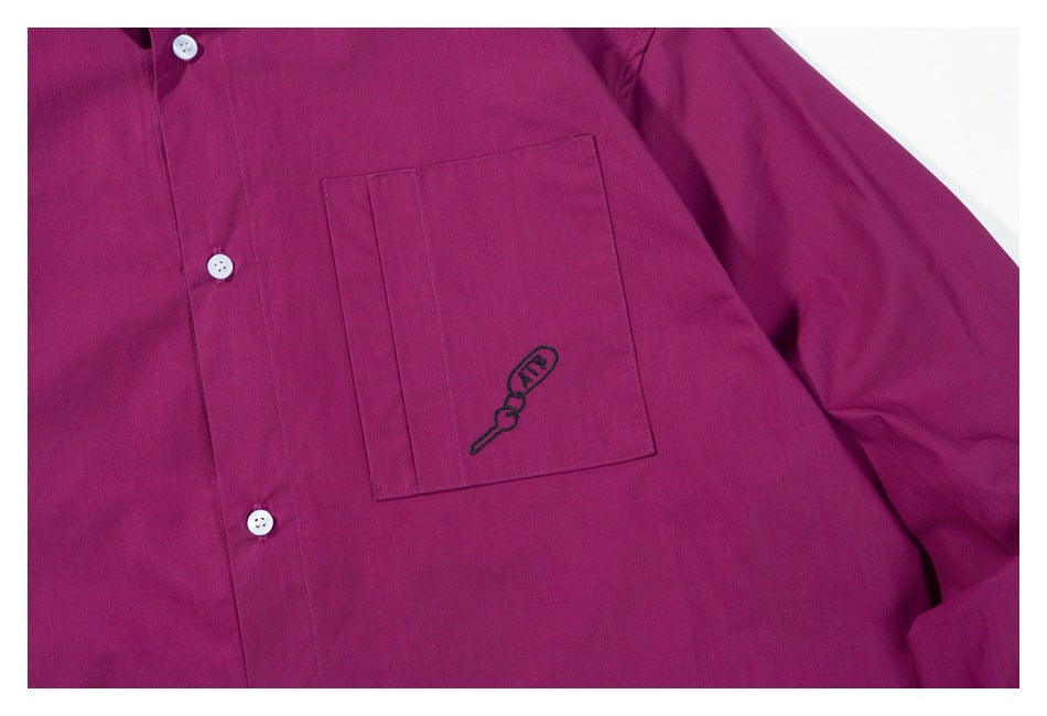 Close-up of the magenta shirt's chest pocket with small black embroidered artwork and white buttons.