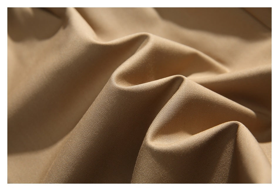 Close-up of tan trouser fabric draped into soft folds, showing its fine surface texture.