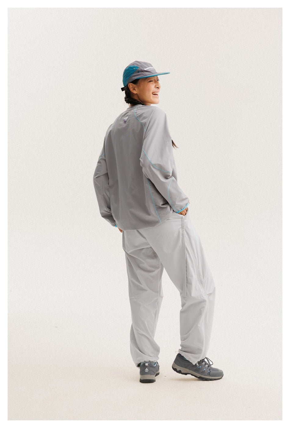 Model turned to show the back of a gray long-sleeve top with turquoise piping and matching pants.