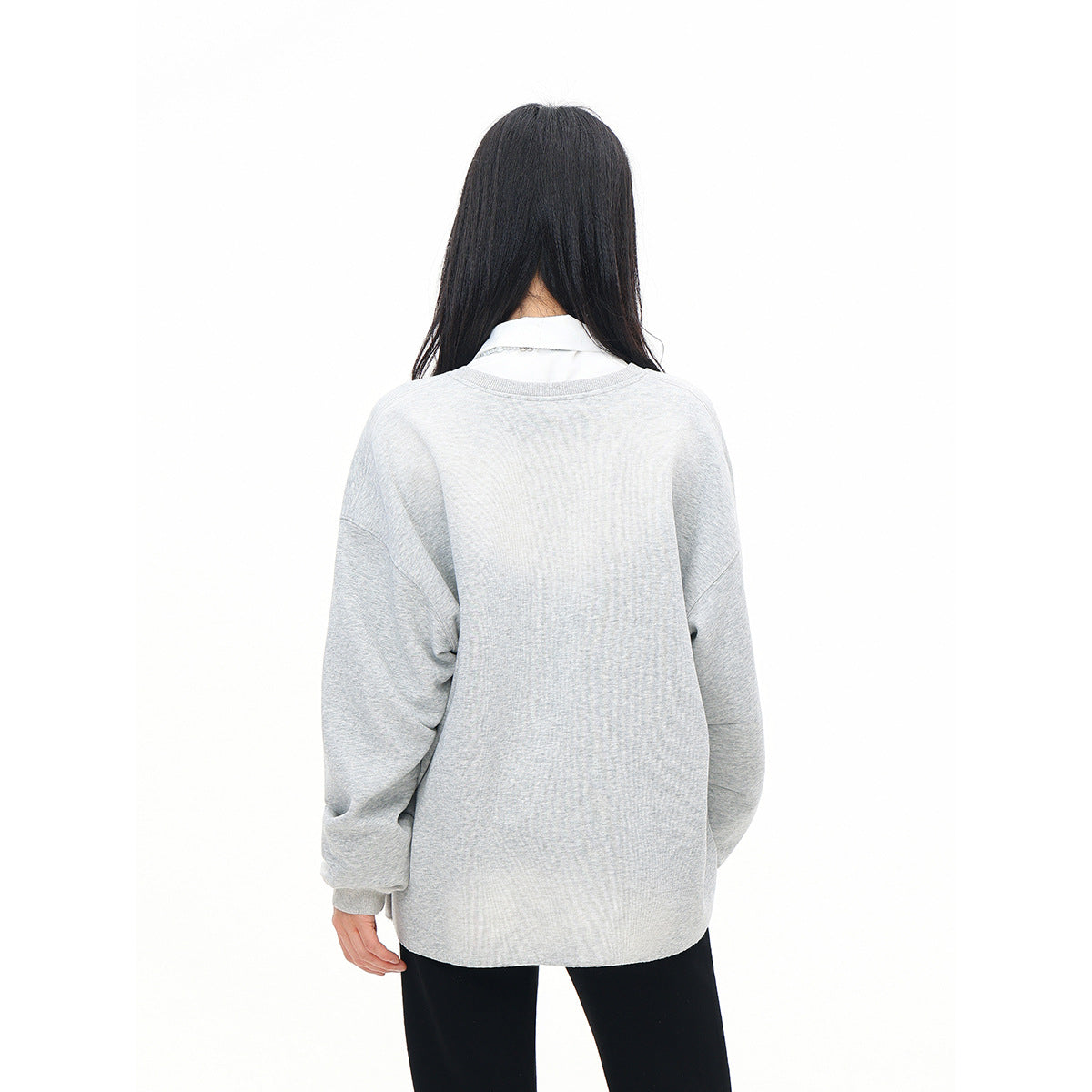 Rear view of a model wearing an oversized plain light gray sweatshirt with dropped shoulders and ribbed cuffs.
