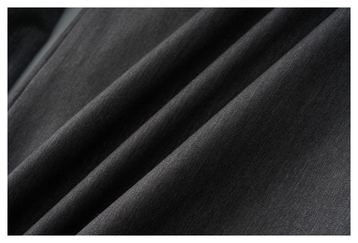 Close-up of dark charcoal fabric with soft diagonal folds and a fine surface texture.