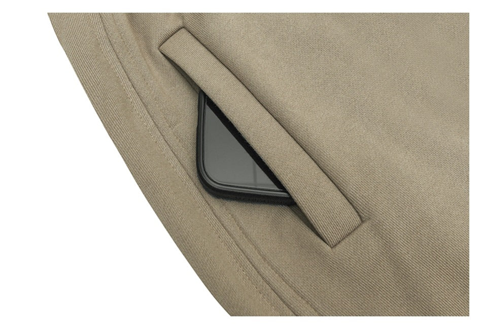 Close-up of taupe trousers showing a slanted welt pocket with a phone tucked inside.