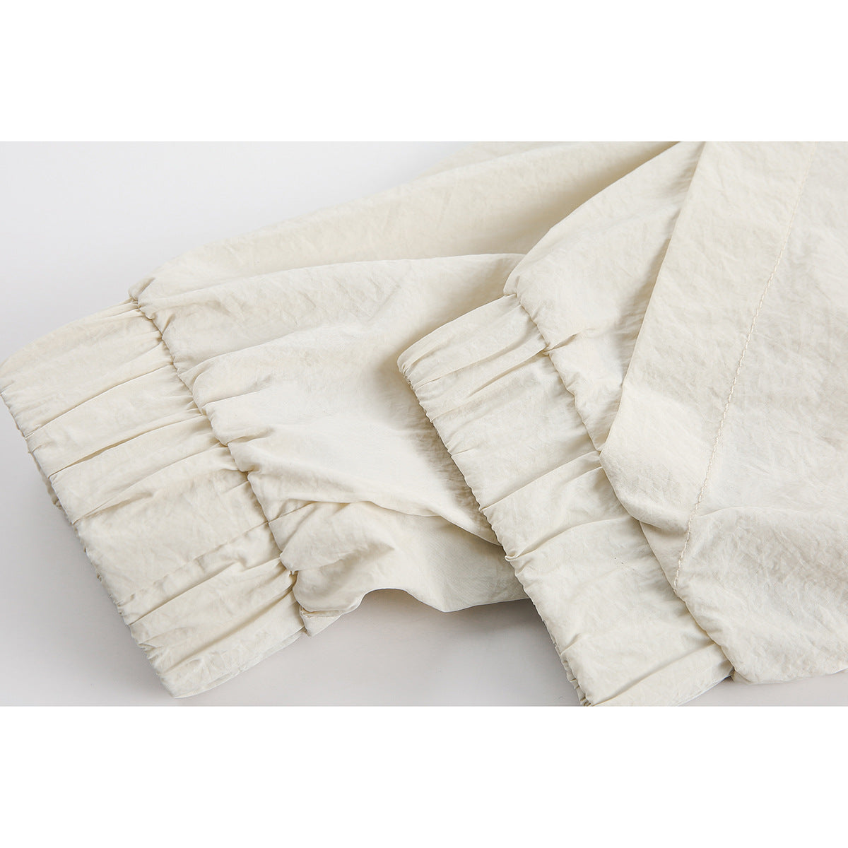 Close-up of ivory jacket fabric and gathered sleeve cuffs, with part of the hood visible.