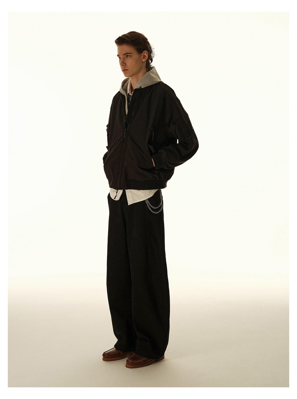 Three-quarter side view of a model in a black zip bomber jacket and wide black trousers.