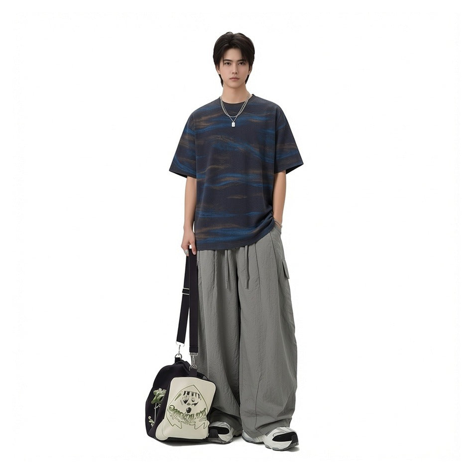 Person wearing gray wide-leg cargo pants with a printed tee, chain necklace and duffel bag