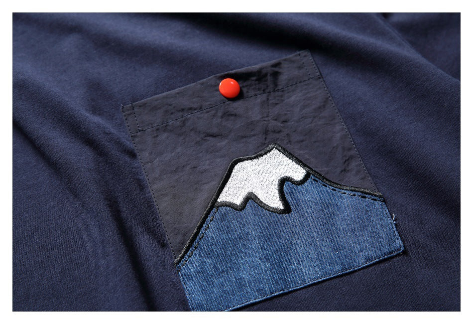 Close-up of the shirt's patch pocket, featuring a blue-and-white mountain appliqué and red button.