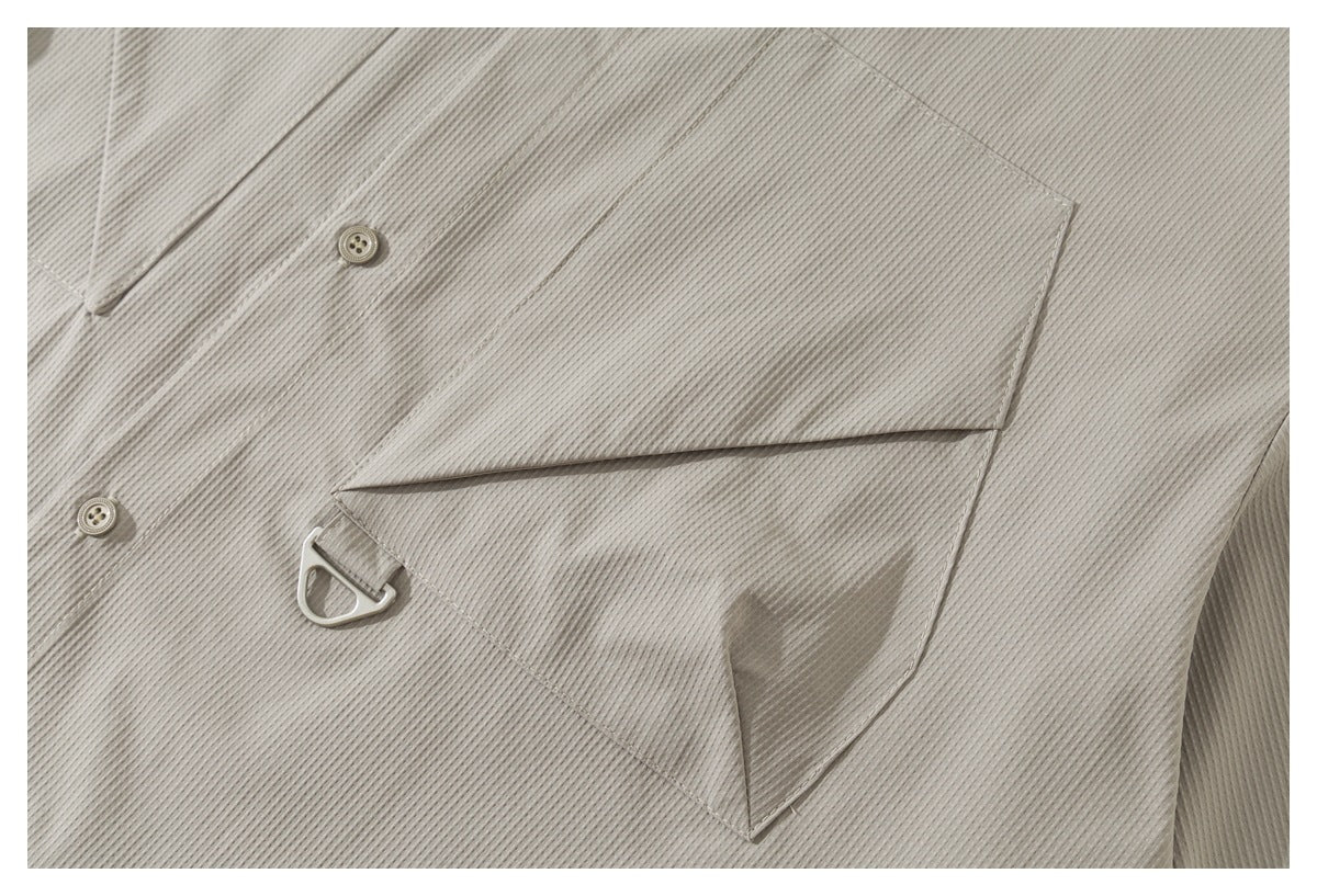 Close-up of a flap chest pocket with a small metal loop on the light taupe ribbed shirt.