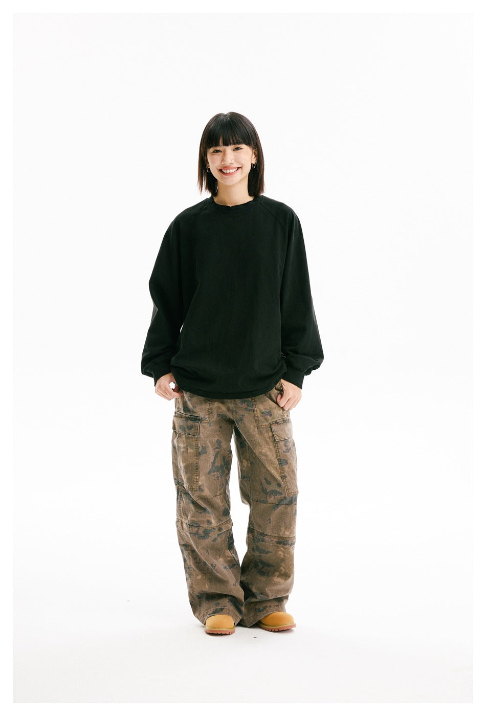 Front view of a model wearing an oversized black crewneck sweatshirt and brown camouflage cargo pants.