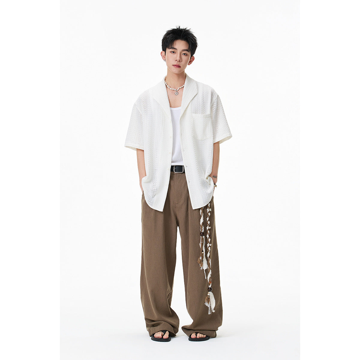 Model wearing a white short-sleeve textured button-up shirt with a chest pocket and wide brown trousers.
