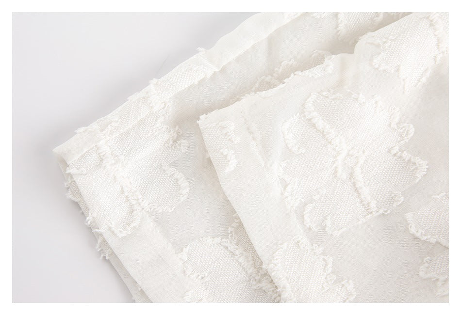 Close-up of ivory fabric with raised floral motifs and layered finished edges.