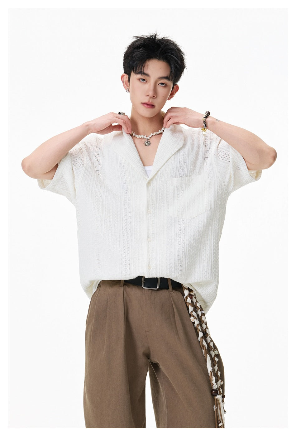 Model holding the collar of a white openwork short-sleeve shirt, showing its shawl collar, buttons, and chest pocket.