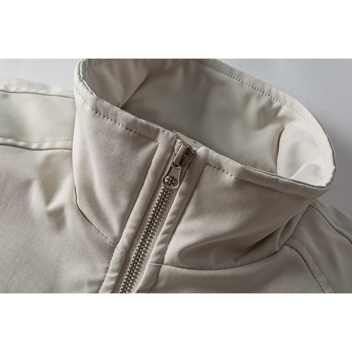 Close-up of a light beige jacket's tall collar and metal front zipper.