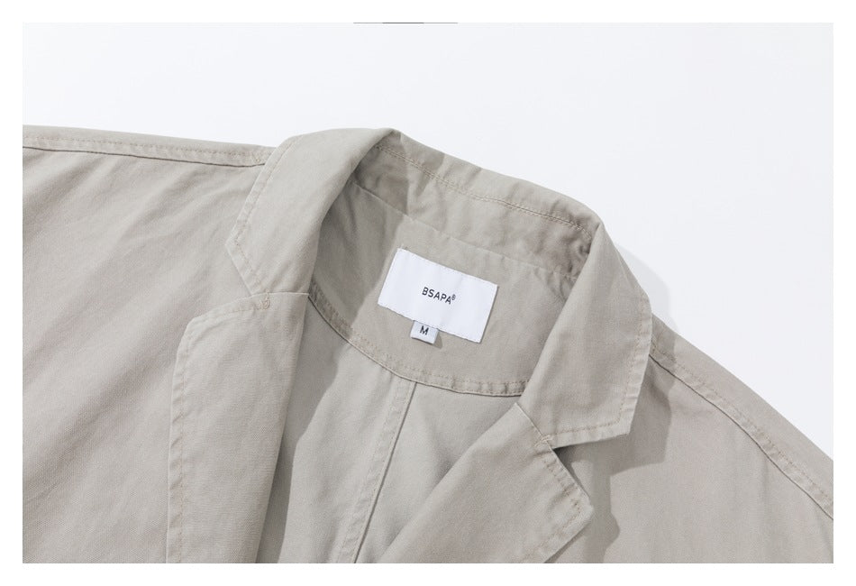 Close-up of a light gray-beige jacket's notched lapel and sewn neck label marked BSAPA, size M.