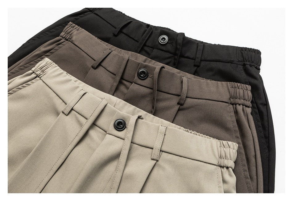 Three pairs of trousers in black, brown, and taupe, layered to show elastic waists, buttons, and belt loops.