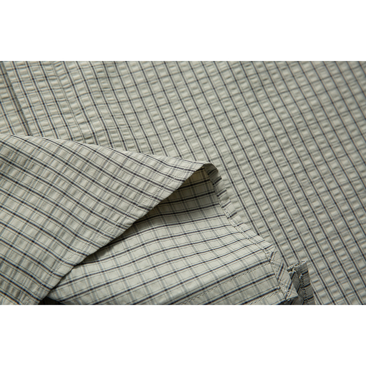 Close-up of the pale gray-green plaid shirt fabric and a folded seam.