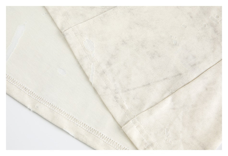 Close-up of an ivory garment's overlocked hem and seam against mottled distressed fabric.