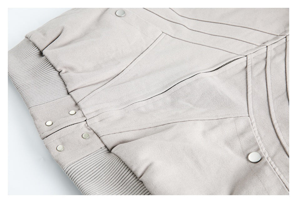 Close-up of a beige jacket panel with ribbed trim, stitched seams, and several snap fasteners.