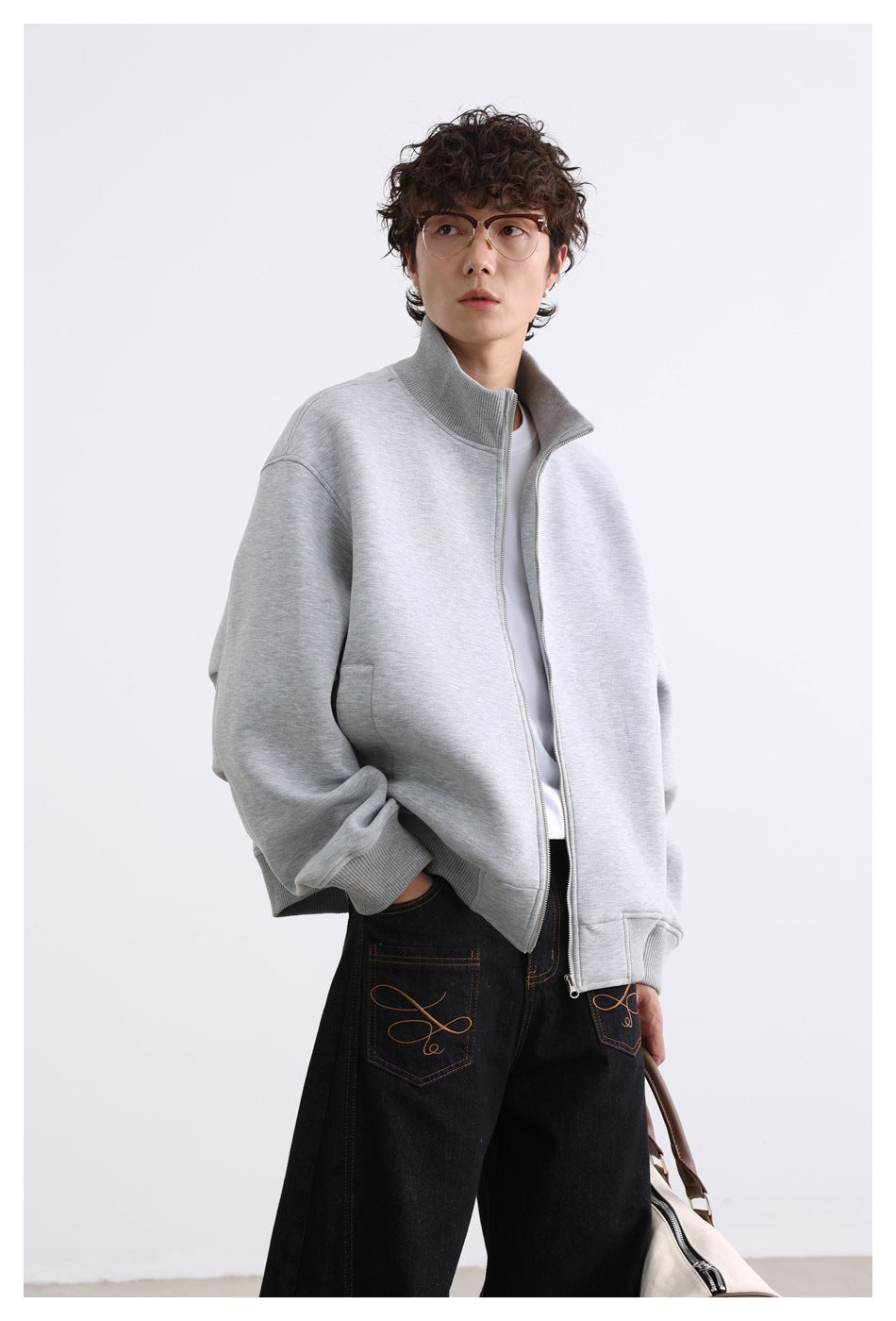 Closer view of a model wearing a light gray zip jacket with a stand collar and ribbed cuffs.