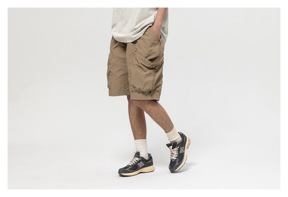 Model wearing taupe cargo shorts, shown from the front and side with sneakers and a large drawcord side pocket.