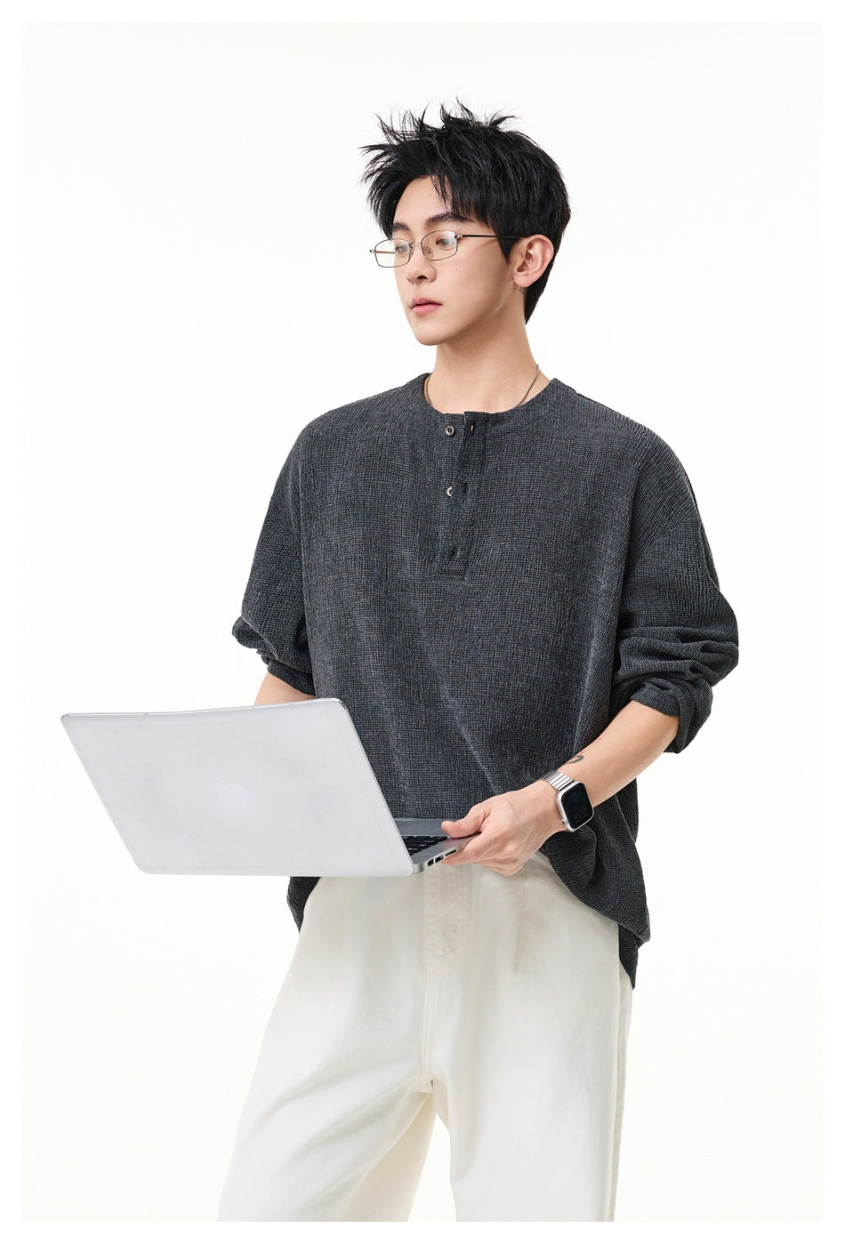 Model wearing a charcoal gray textured henley with rolled sleeves and white trousers, front view.