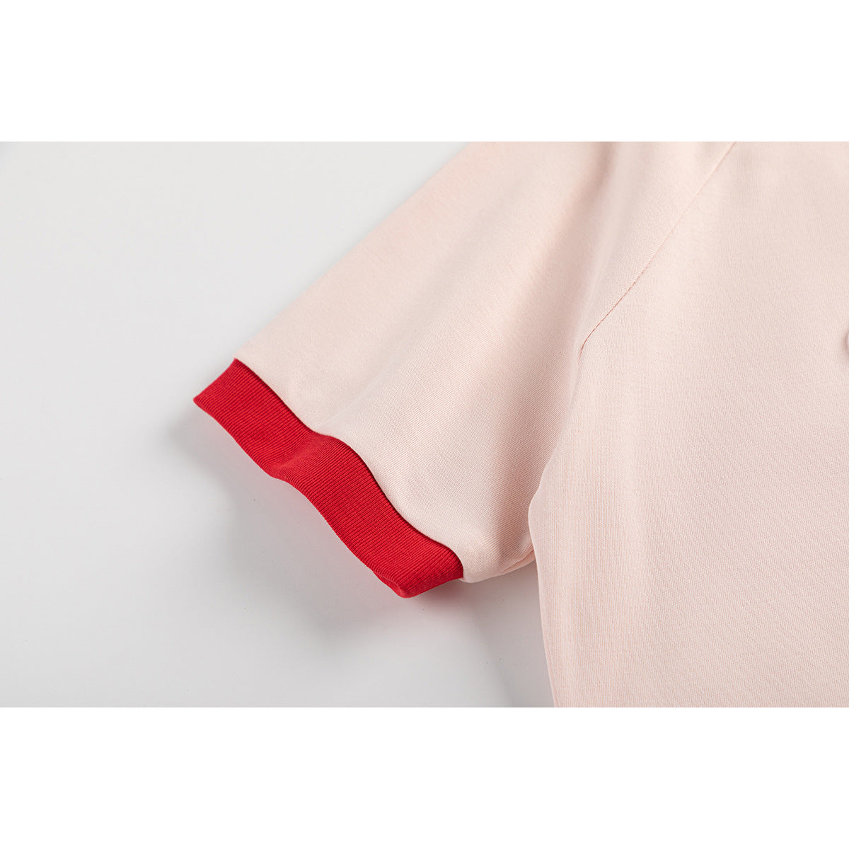 Close-up of a pale pink short sleeve finished with a bright red ribbed cuff.